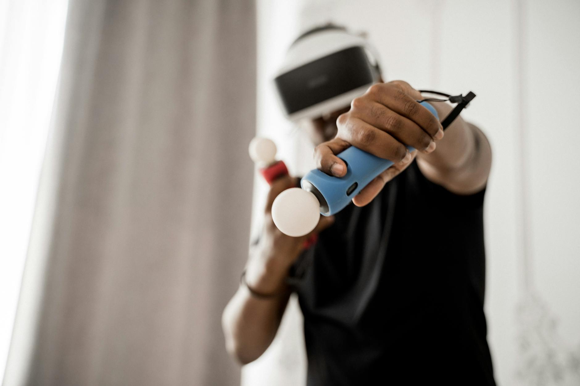 Person using VR headset with motion controllers, engaging in a virtual reality game indoors.
